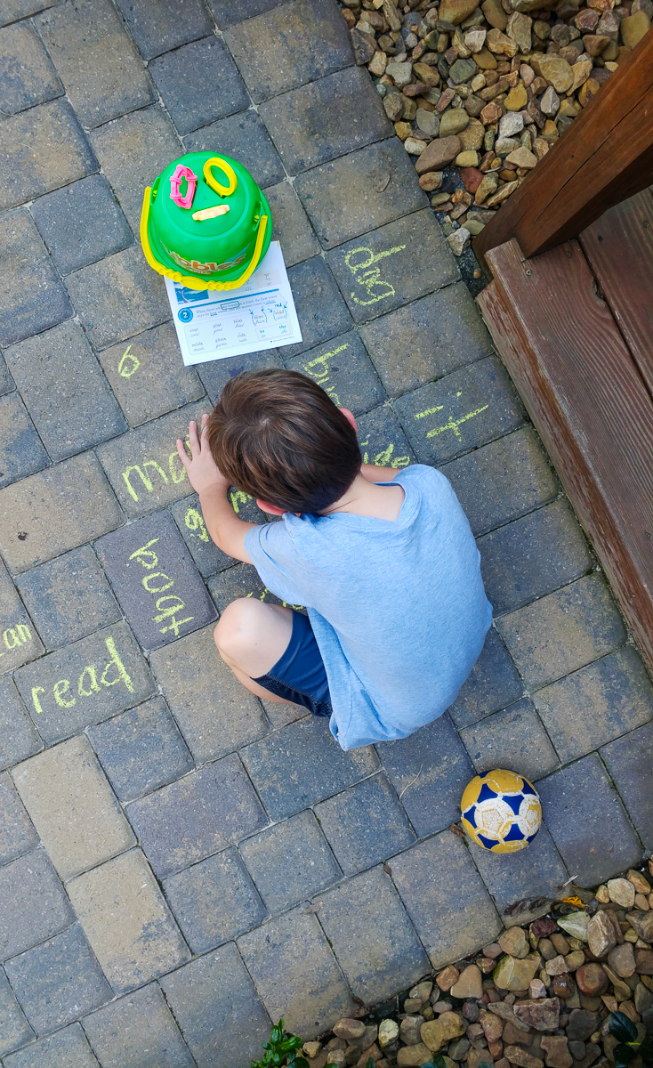 Boy Practicing His Spelling Words Using Sidewalk Chalk to Write