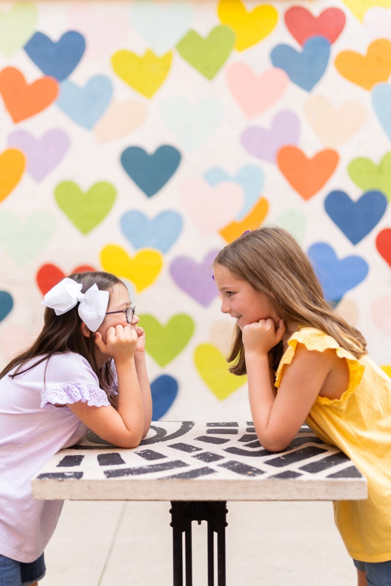 Girls Posing for Photo in Front of Wall of Hearts