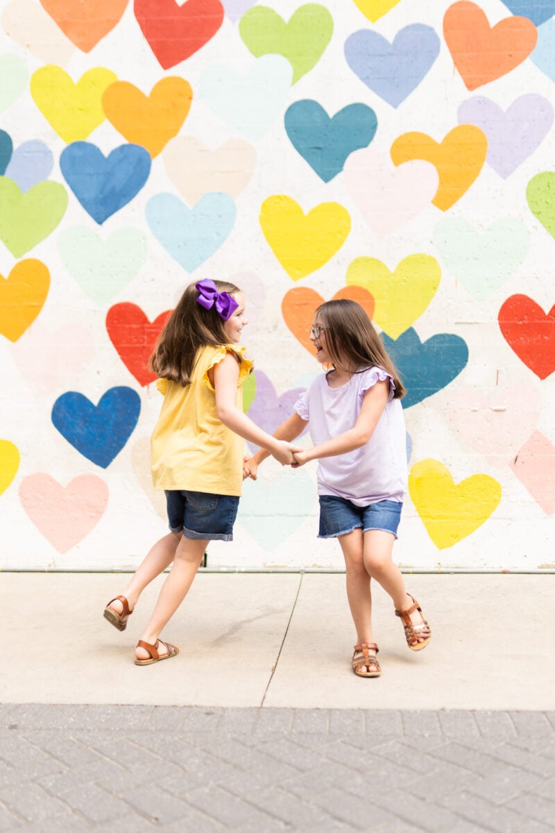 Girls Posing for Photo in Front of Wall of Hearts