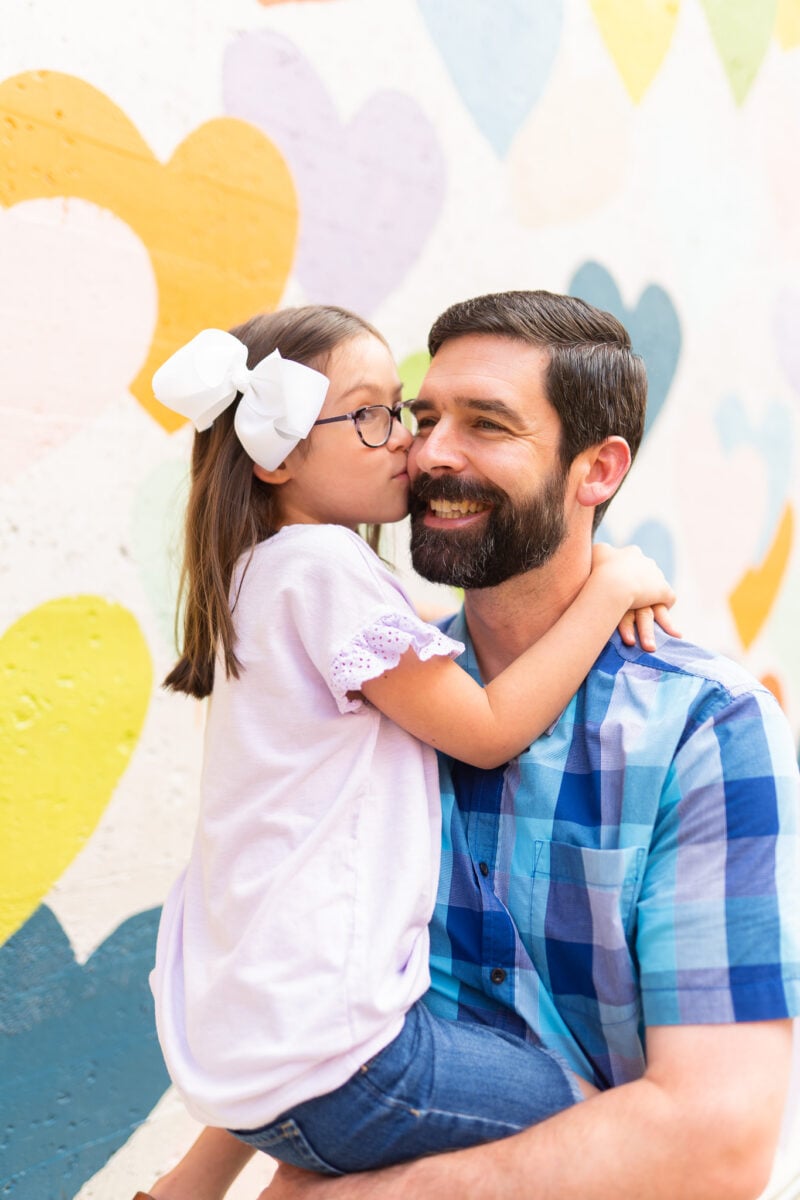 Father and Daughter Posing for Photo in Front of Wall of Hearts