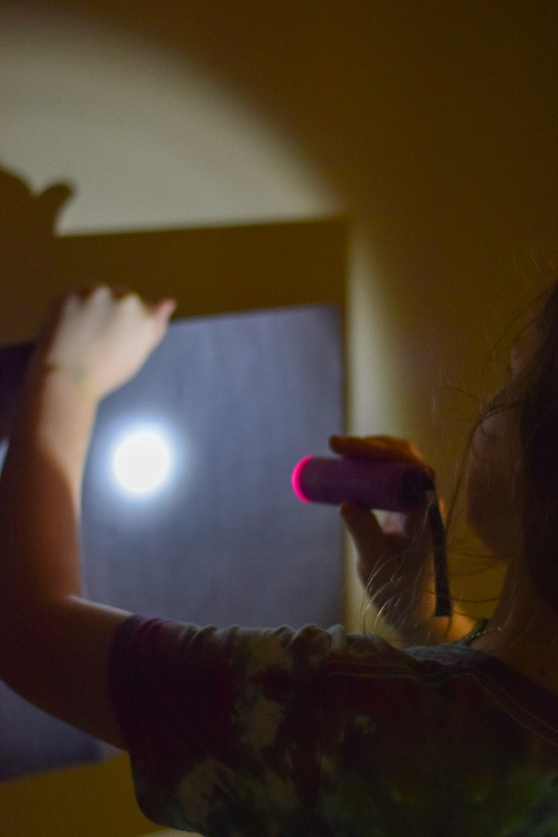Child Shining Flashlight on Black Construction Paper with Holes in It